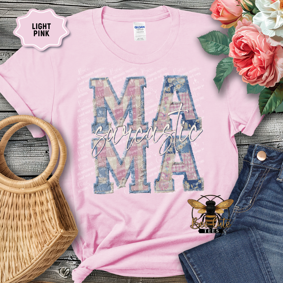 Light pink t-shirt with 'Mama' design, surrounded by flowers and denim jeans on a wooden surface.