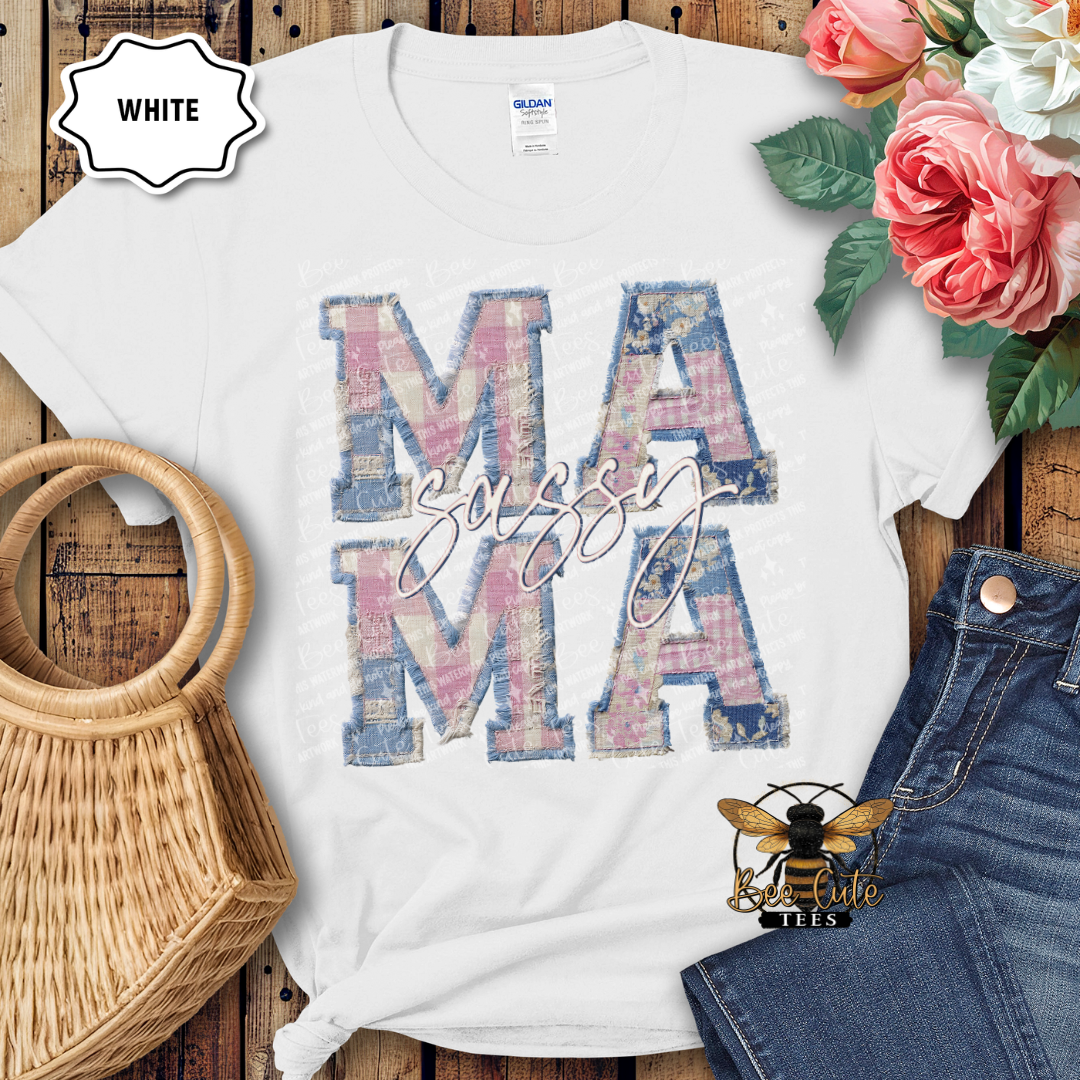 White t-shirt with 'SASSY MAMA' design on a wooden surface with flowers and denim jeans.