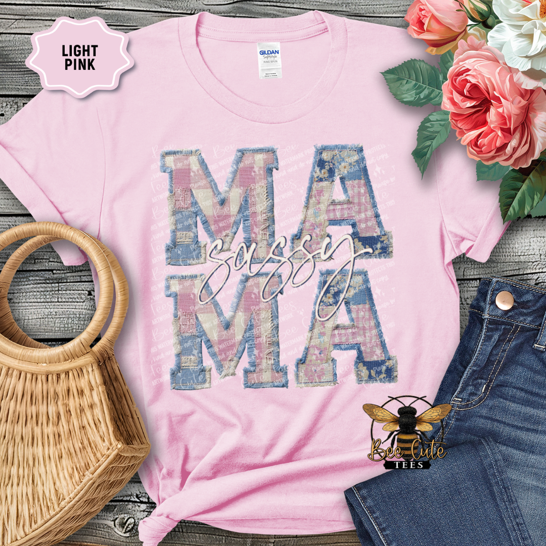 Light pink t-shirt with 'Mama' design on a wooden surface with flowers and denim jeans.