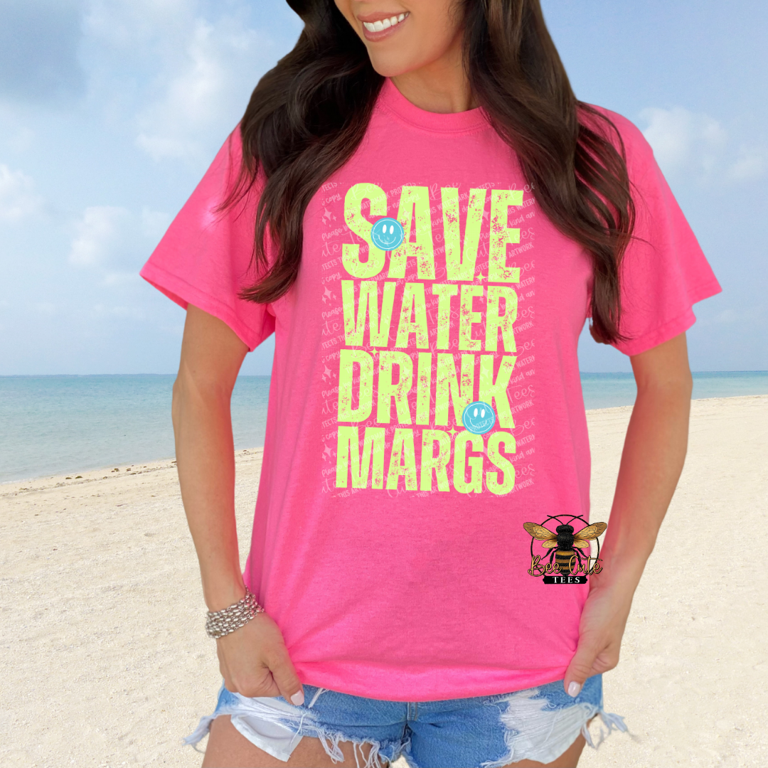 Person wearing a pink t-shirt with 'SAVE WATER DRINK MARGS' text on a beach.