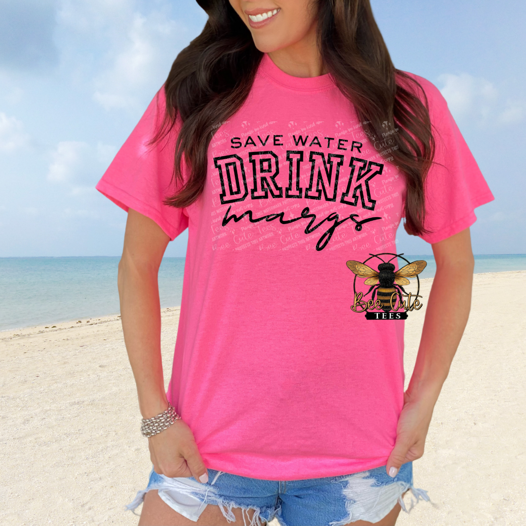 Person wearing a pink t-shirt with 'Save Water Drink Margs' text on a beach.