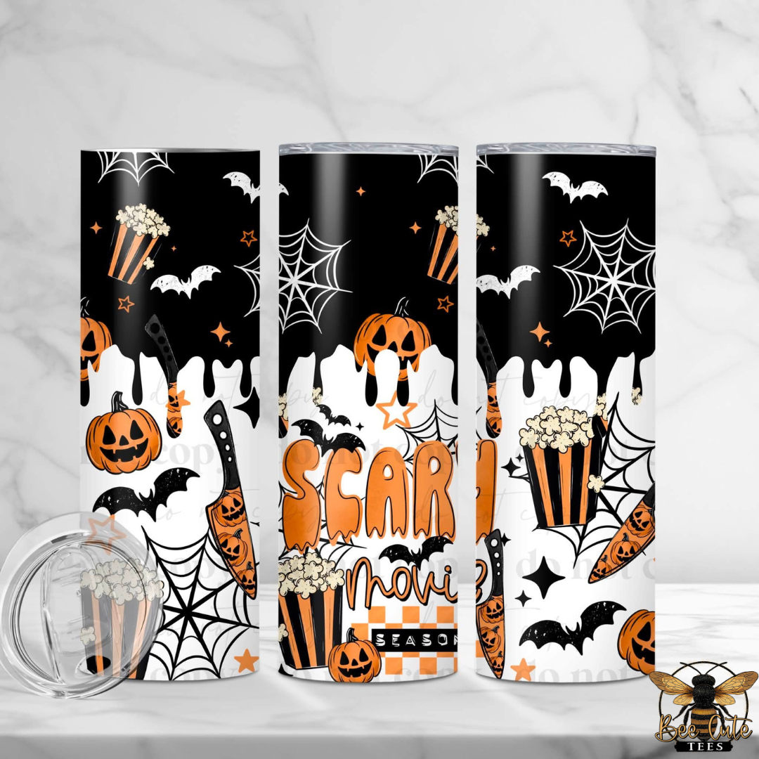 Three slim stainless steel tumblers with a Halloween-themed 'Scary Movie Season' print, displayed on a white marble surface with a clear glass lid in the foreground. The design features a black and white dripping background with orange pumpkins, bats, spiderwebs, popcorn, and stars.