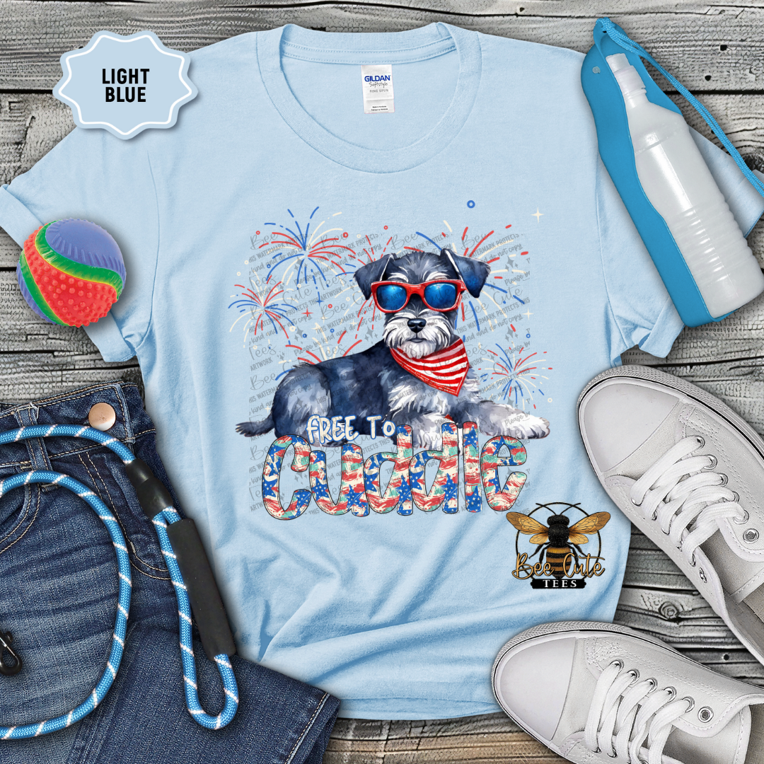 Light blue t-shirt with a dog graphic and text, surrounded by jeans, shoes, and accessories on a wooden surface.