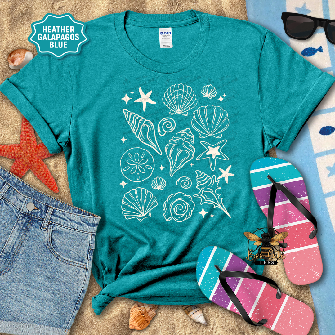 Teal t-shirt with seashell design on a beach-themed background with sunglasses, flip-flops, and starfish.