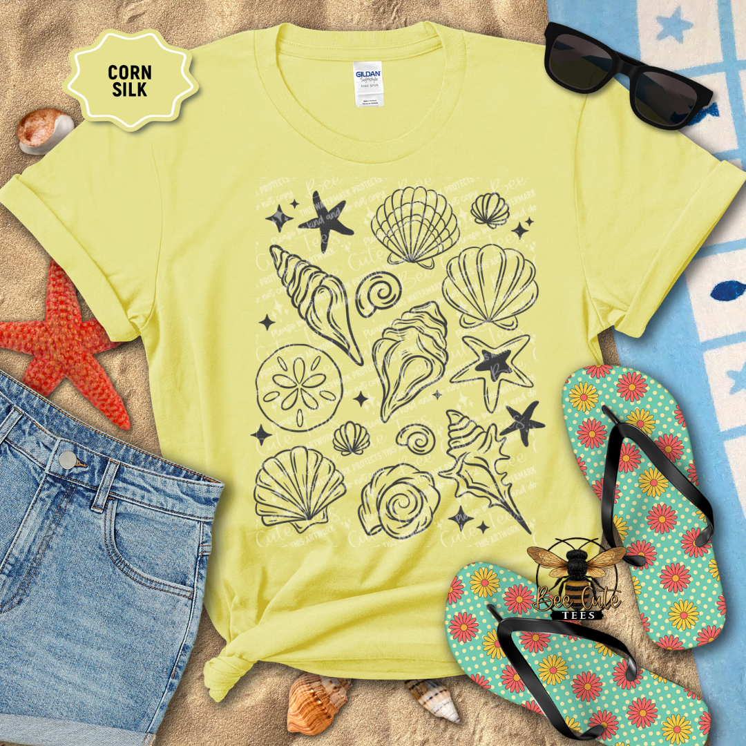 Yellow t-shirt with beach-themed design on a sandy surface with flip-flops and sunglasses.