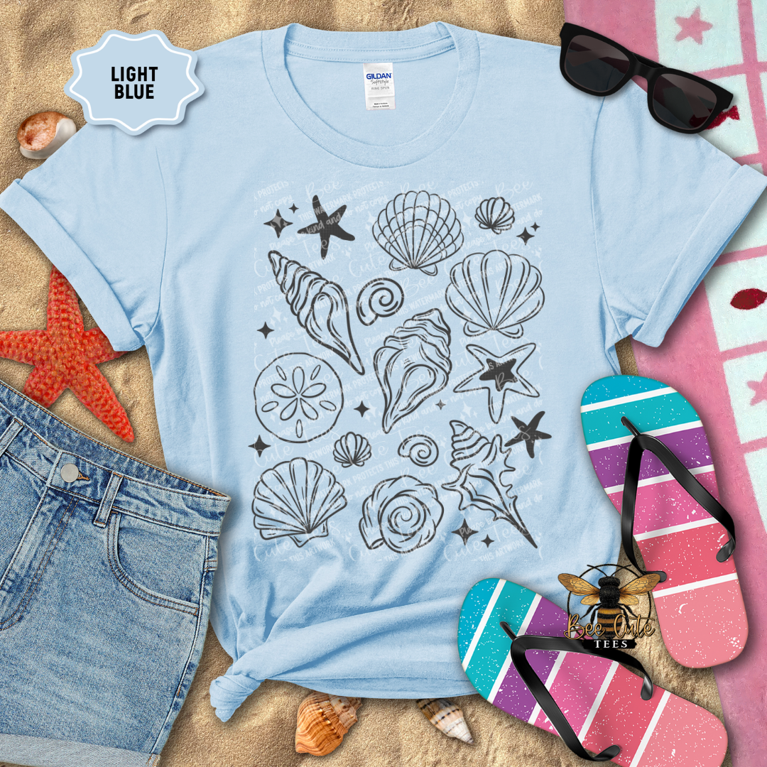 Light Blue t-shirt with beach-themed design on a sandy surface with flip-flops and sunglasses.