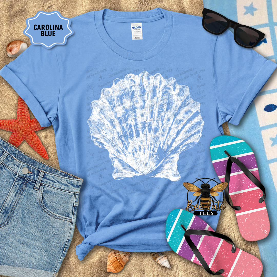 Blue t-shirt with a white shell design, surrounded by beach accessories on a sandy background.