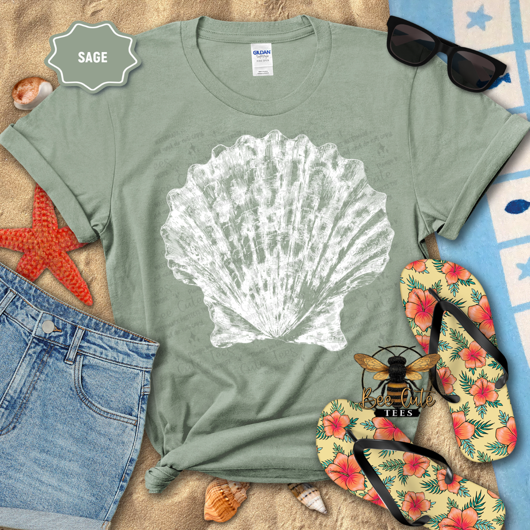 Sage green t-shirt with a white shell design on a beach-themed background with flip-flops and sunglasses.