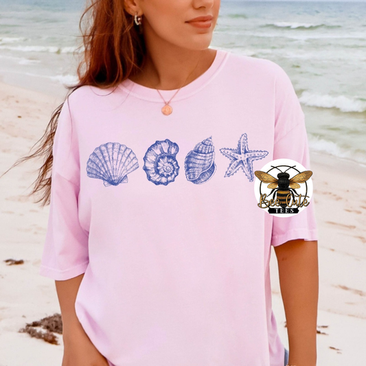 Person wearing a pink shirt with shell and starfish designs on a beach.