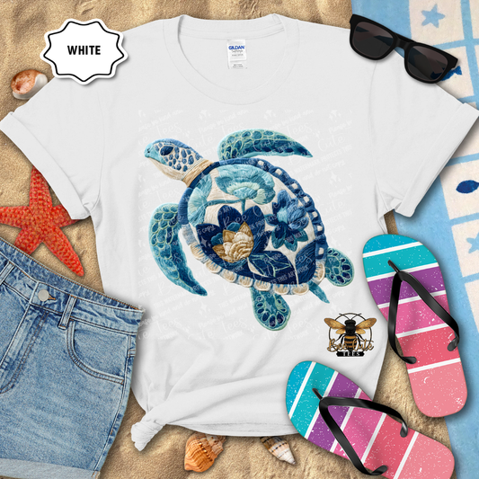 White t-shirt with a blue turtle design, sunglasses, and flip-flops on a beach-themed background.