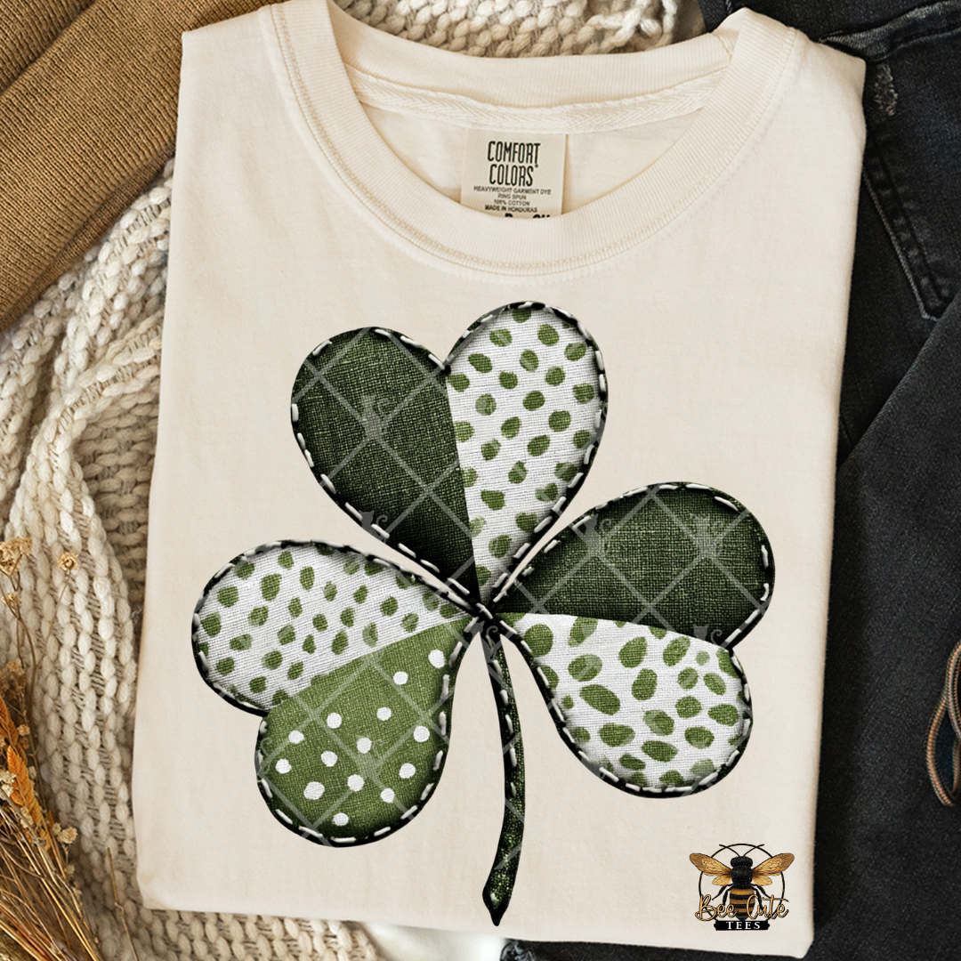 Folded white t-shirt with a green and white four-leaf clover design on a textured surface.