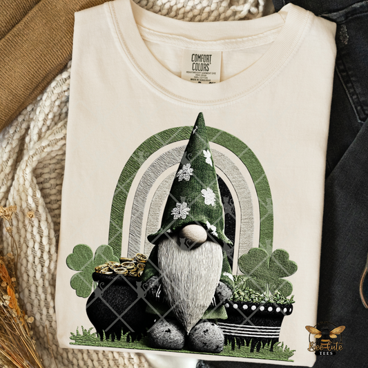 Folded white t-shirt with a gnome and pot of gold design on a textured surface.