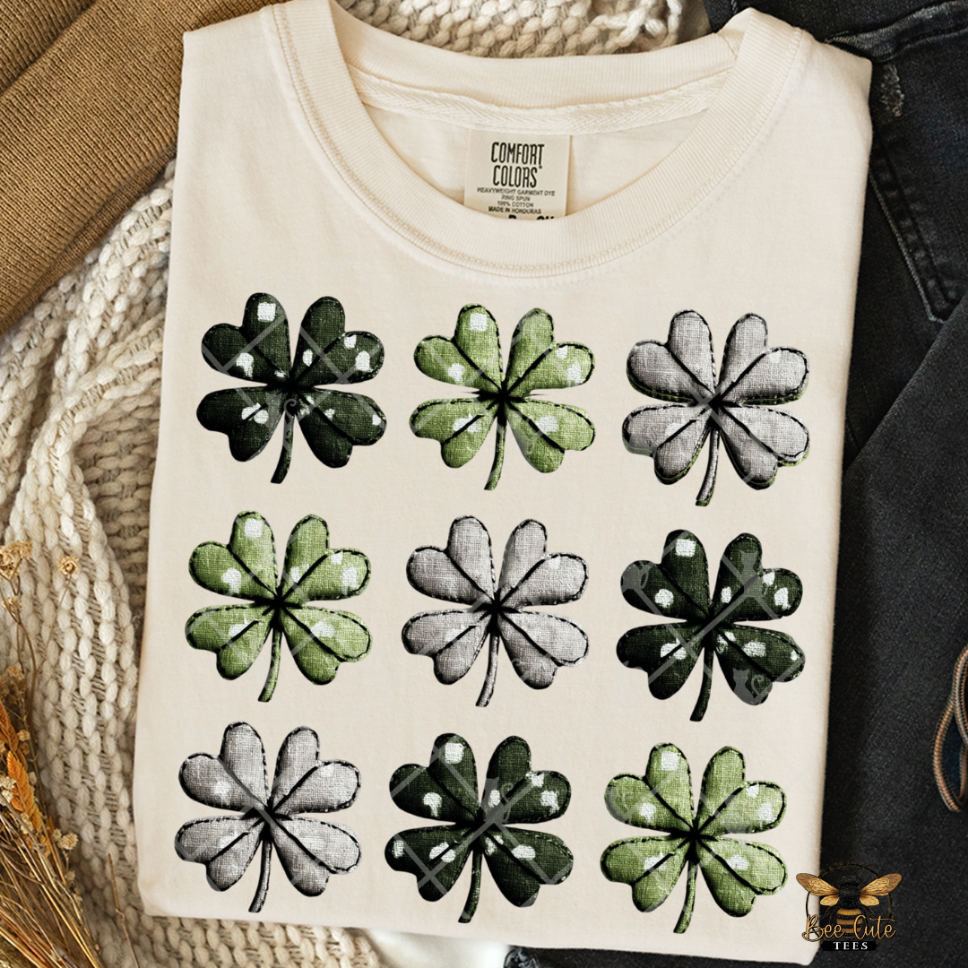 Folded white t-shirt with black and green four-leaf clover pattern on a textured surface.