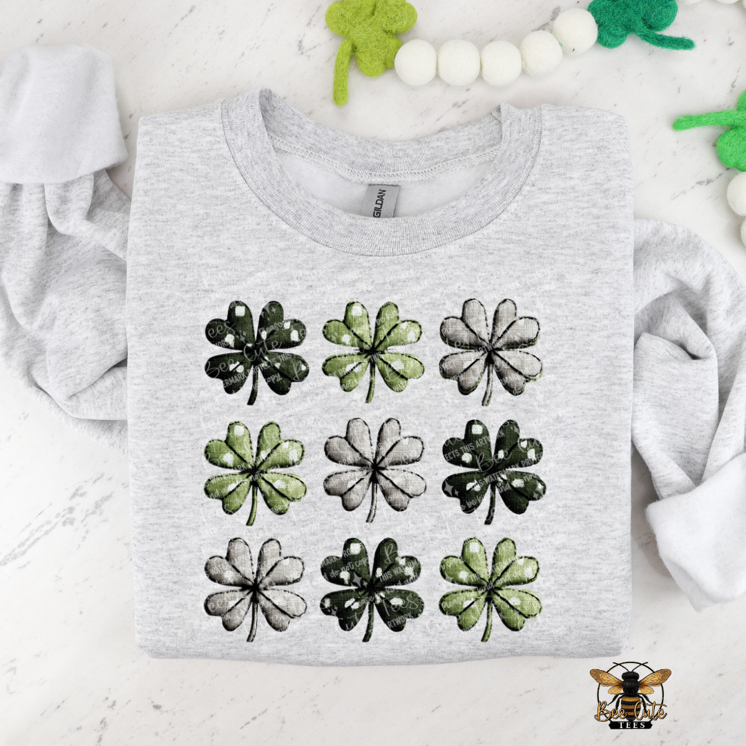 Gray t-shirt with green four-leaf clover patterns on a white background