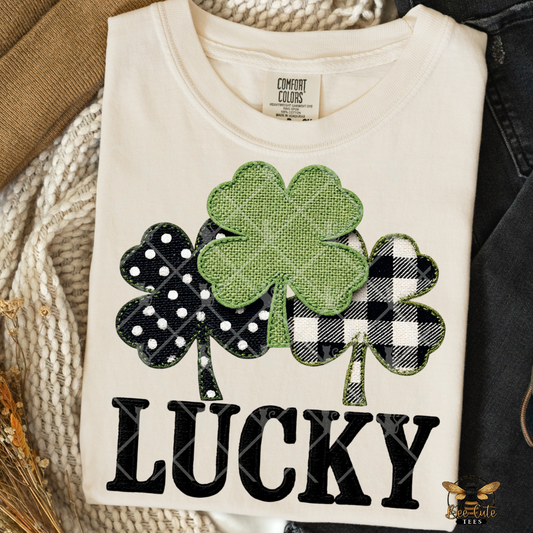 White t-shirt with green shamrock design and 'LUCKY' text on a textured surface.