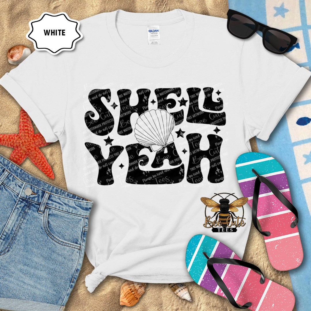 White t-shirt with 'Shell Yeah' design on a beach-themed background with flip-flops and sunglasses.