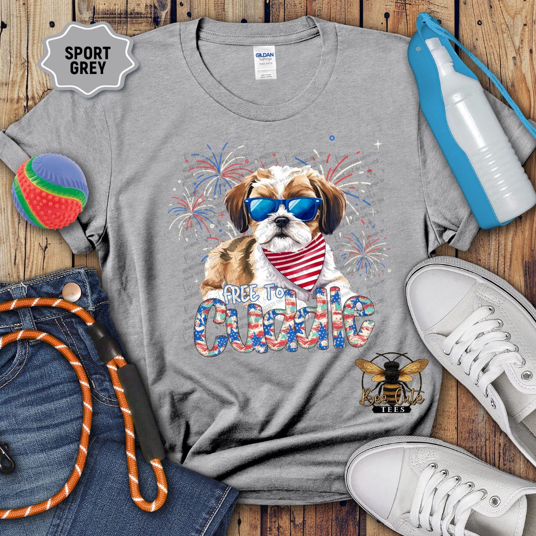 Gray t-shirt with a dog graphic and 'Free To Cuddle' text, surrounded by casual items on a wooden surface.
