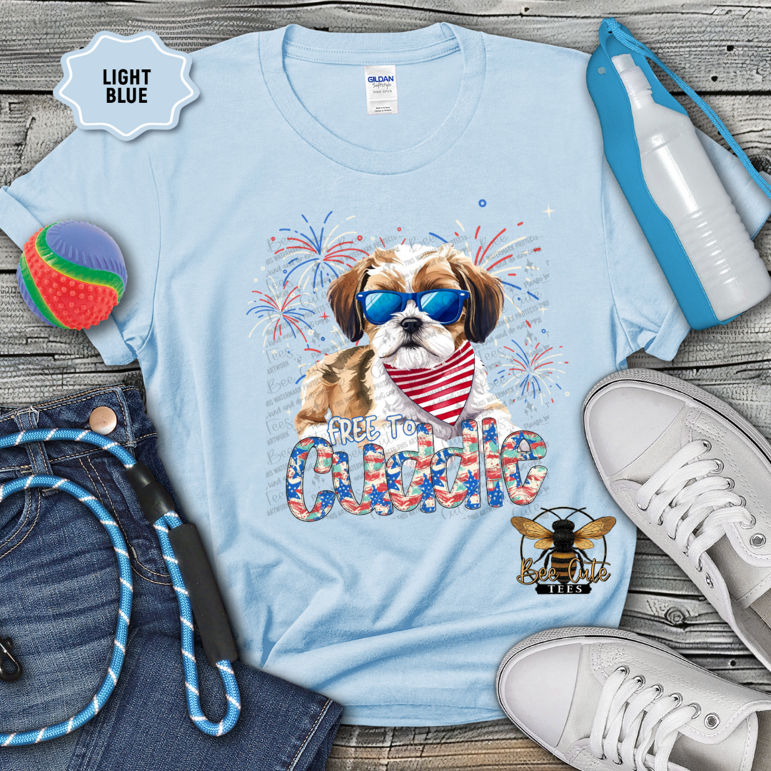 Light blue t-shirt with a dog graphic and 'Free to Cuddle' text, surrounded by accessories on a wooden surface.