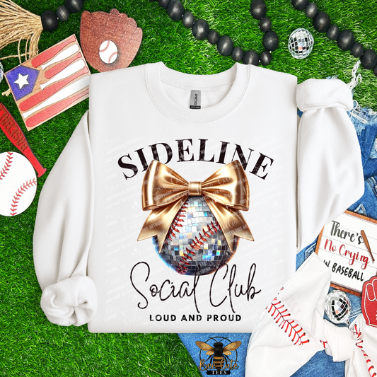 White sweatshirt with 'Sideline Social Club Loud and Proud' design on a grass background with sports-themed accessories.