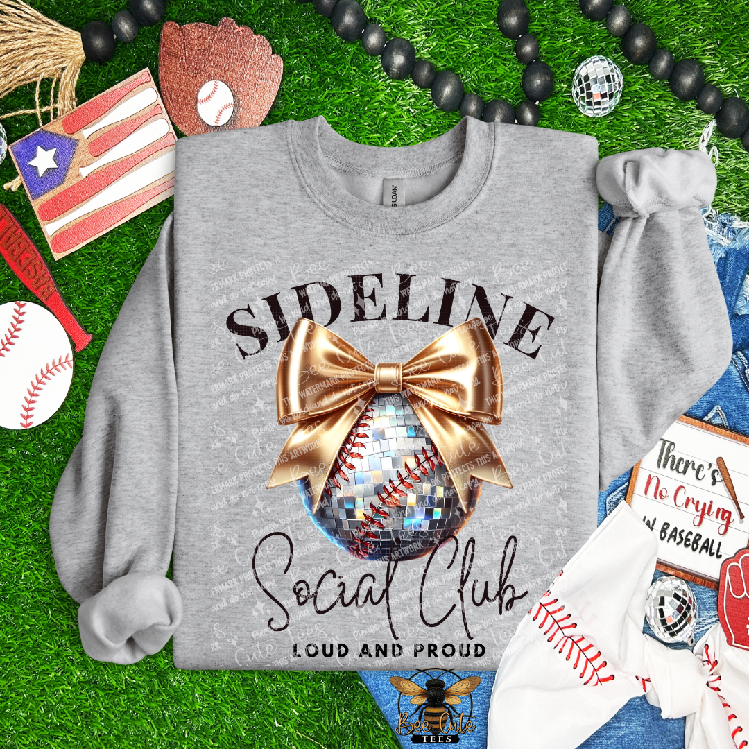 Gray sweatshirt with 'Sideline Social Club Loud and Proud' design on grass with sports-themed accessories.
