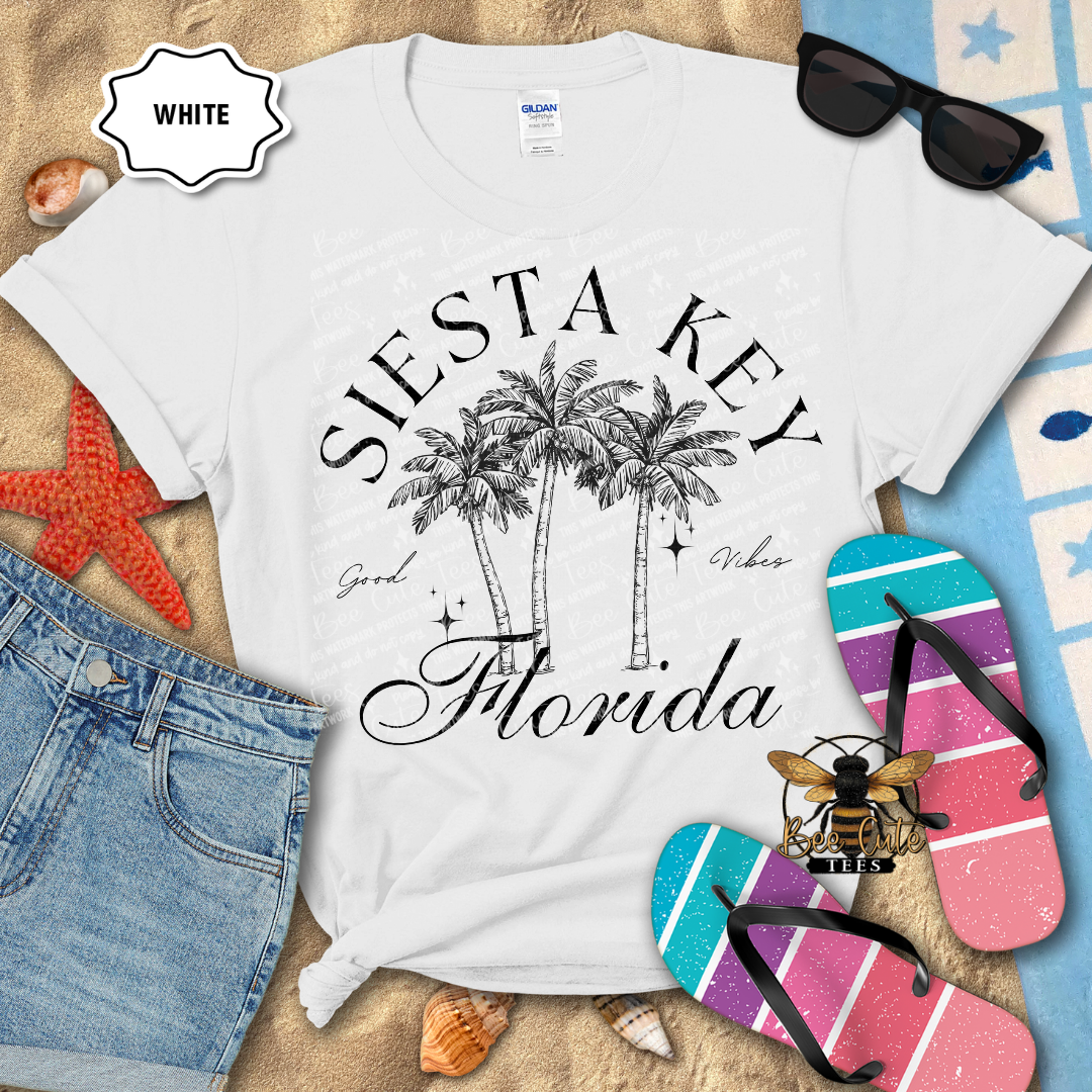 White t-shirt with 'Siesta Key, Florida' design on a beach-themed background with flip-flops and sunglasses.