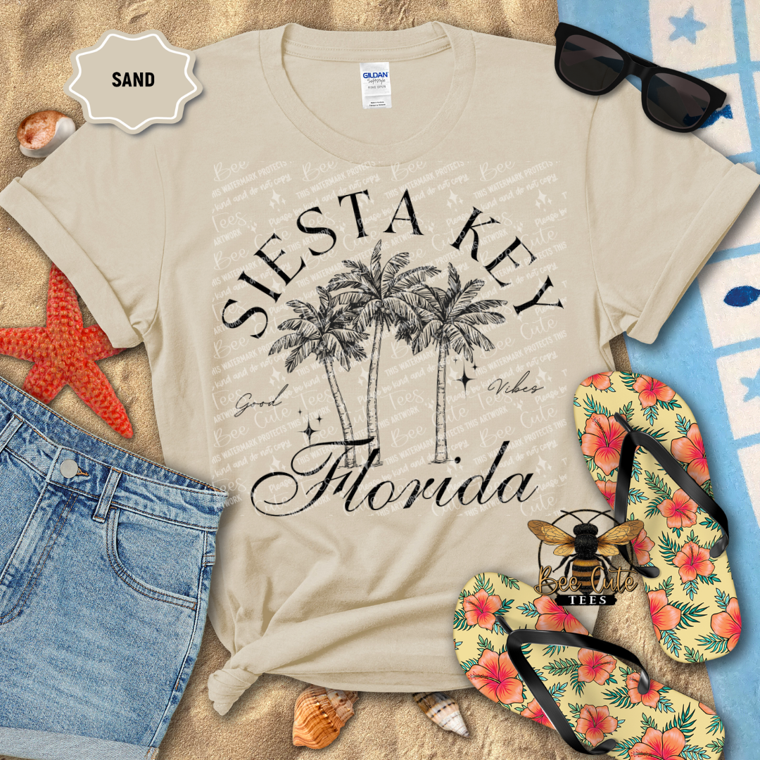 Beige t-shirt with 'Siesta Key Florida' design on a sandy background with beach accessories.