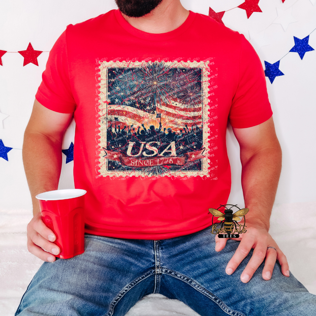 Person wearing a red t-shirt with 'USA Since 1776' design, holding a red cup against a white background with blue and red stars.