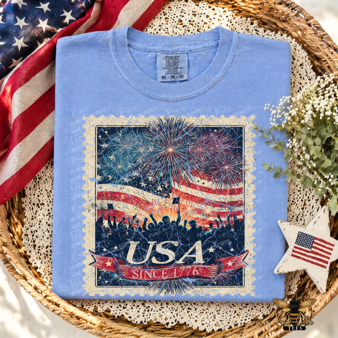 Blue t-shirt with American flag and fireworks design on a woven tray with decorative elements.