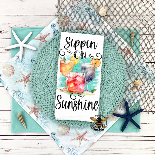 Tea towel with 'Sippin' on Sunshine' text and beach-themed design elements on a textured surface.