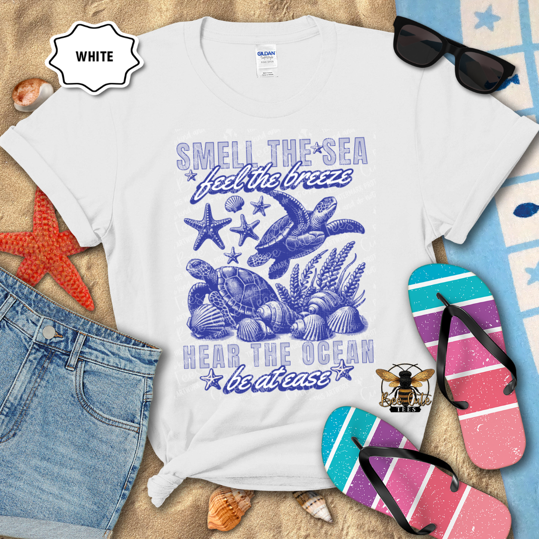 White t-shirt with ocean-themed design and beach accessories on a sandy background