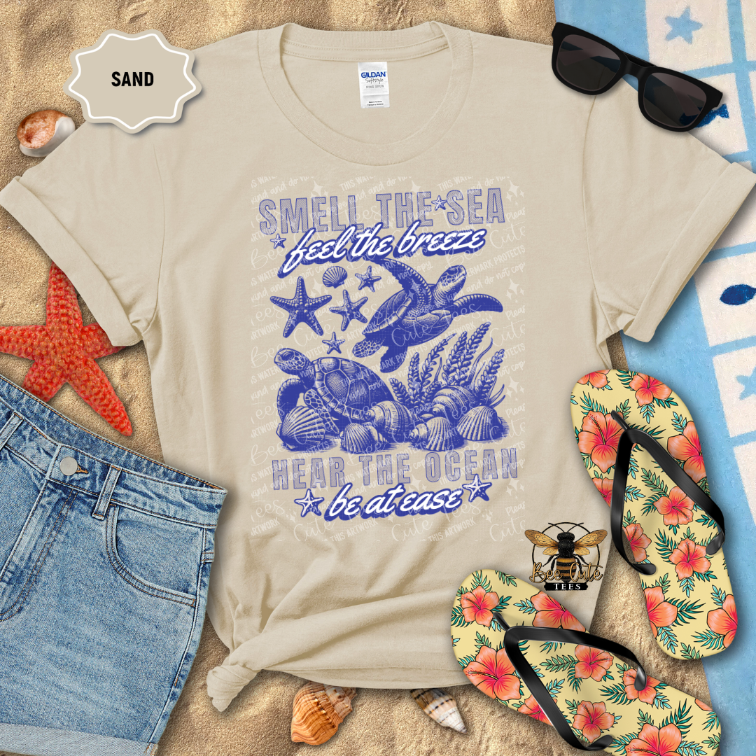 Beige t-shirt with ocean-themed design on a sandy background with beach accessories.