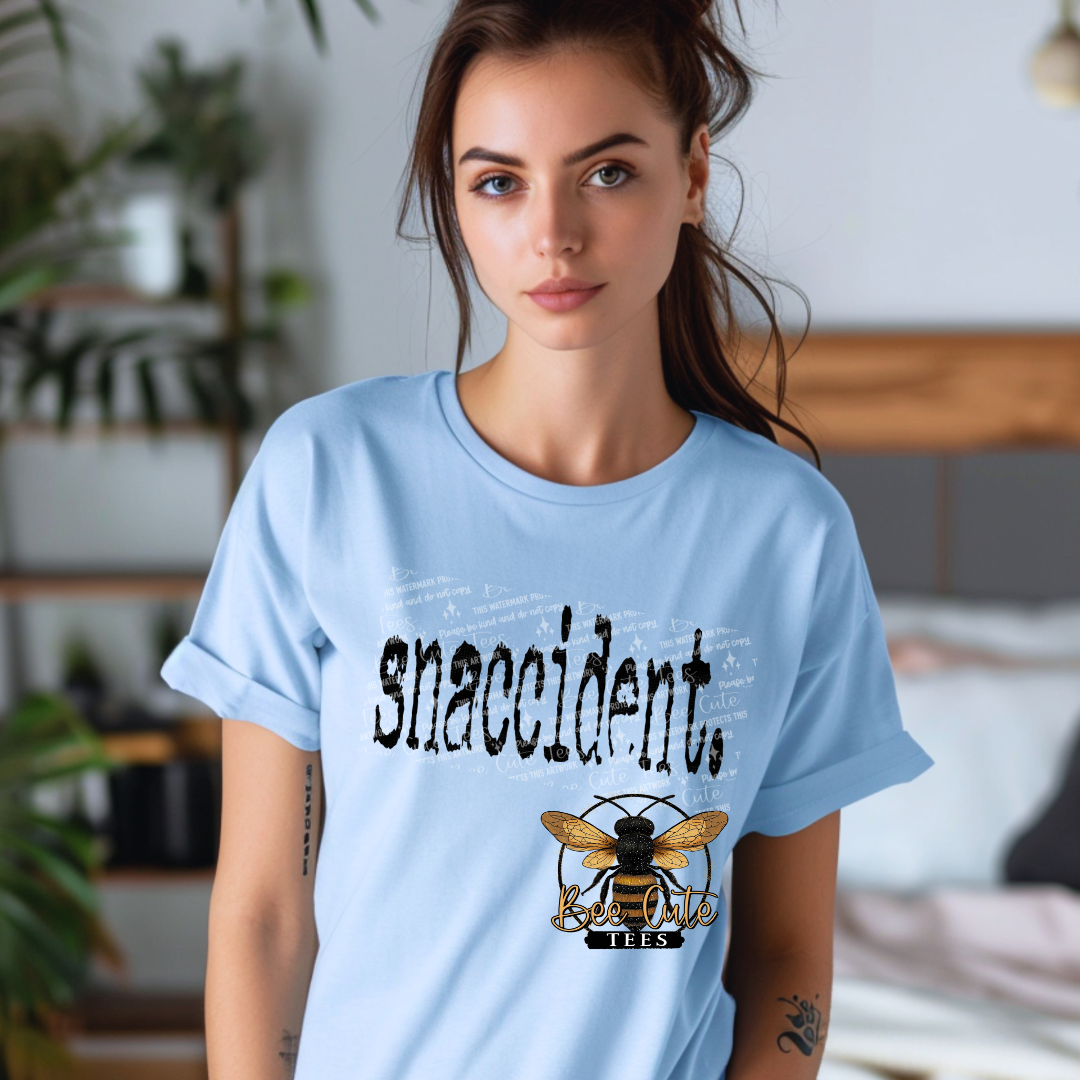 Woman wearing a light blue t-shirt with 'snaccidents' and a bee logo in a casual setting.