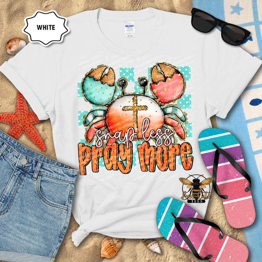 White t-shirt with crab design and text 'Shap less Pray more' on a beach-themed background.