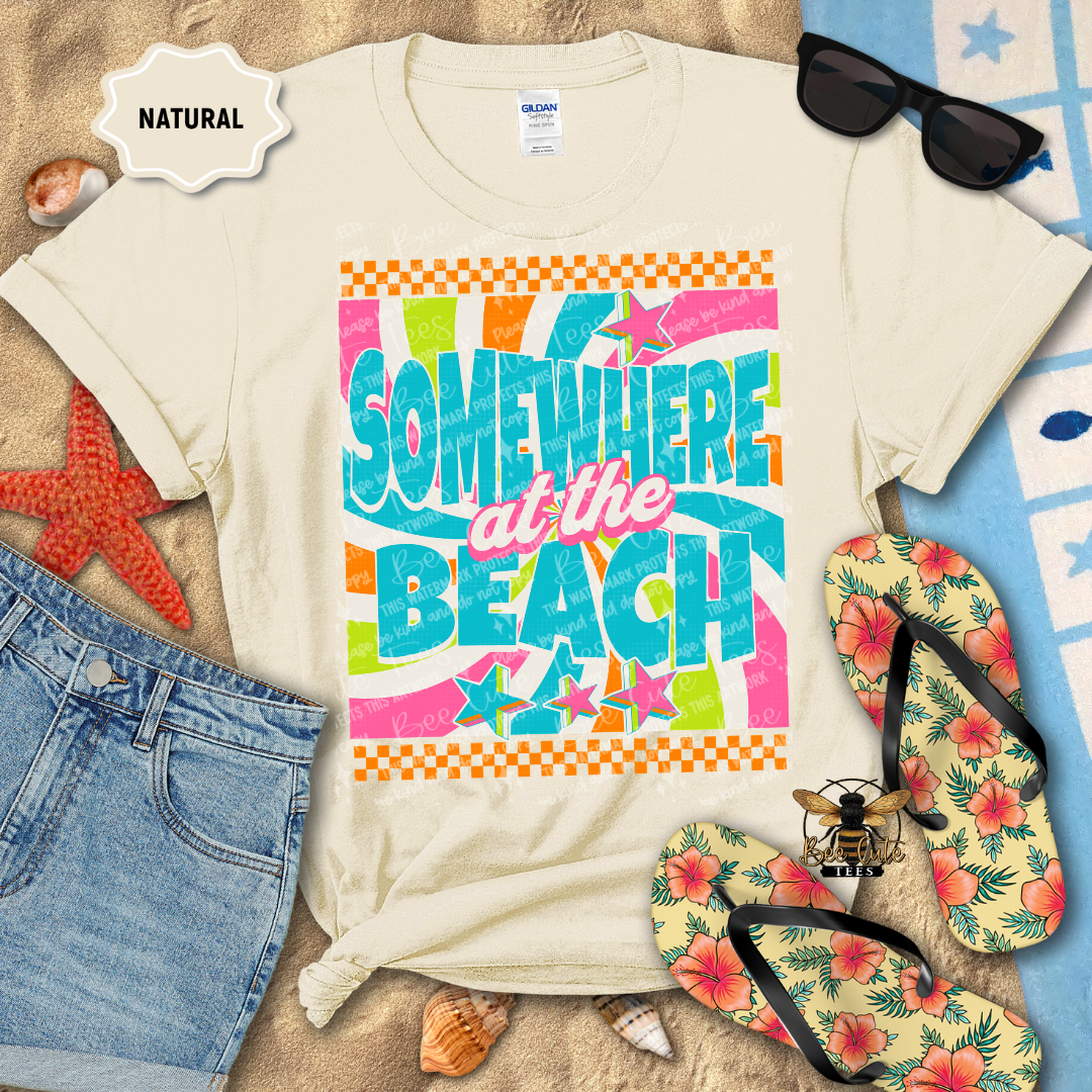 Beach-themed t-shirt with colorful text, sunglasses, flip-flops, and beach accessories on a sandy background.