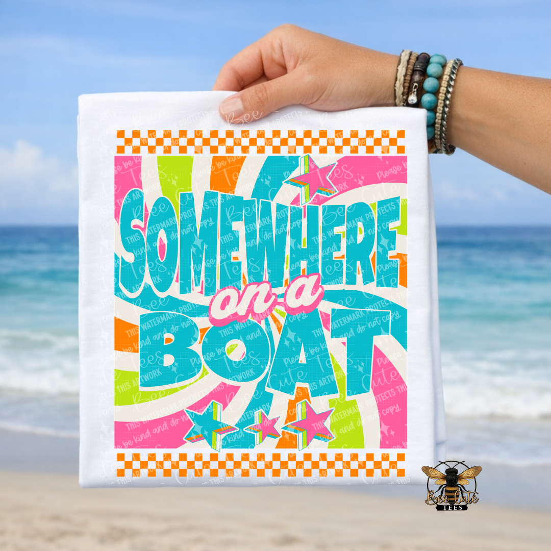 Colorful t-shirt with 'Somewhere on a Boat' text held by a hand against a beach background