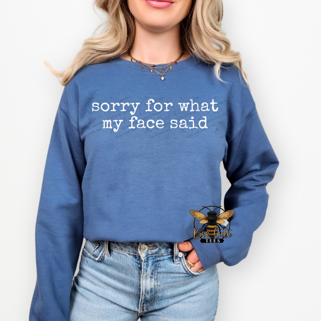 Person wearing a blue sweatshirt with text 'sorry for what my face said' on a white background
