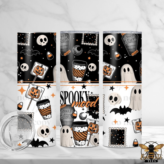 Three tall skinny tumblers with a Halloween-themed pattern, shown on a white marble surface with a clear lid in the foreground. The design features black, white, and orange motifs including skulls, ghosts, pumpkins, bats, stars, and candy corn, with 'Spooky mood' text on the center tumbler.