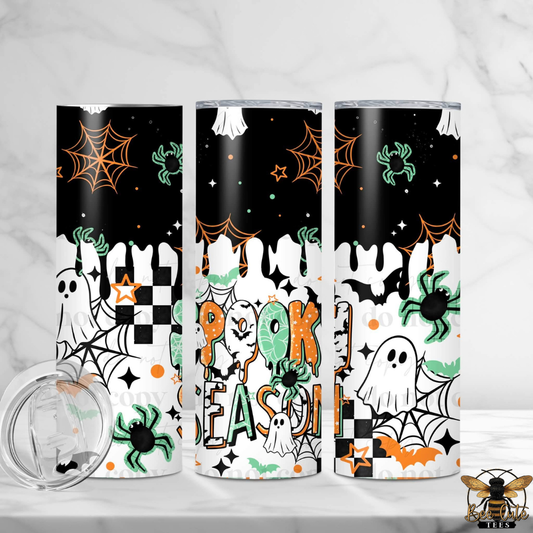 Three slim tumblers with a Halloween-themed print are displayed on a white marble surface. The design features a black and white dripping pattern with orange spiderwebs, green spiders, ghosts, bats, stars, and the words 'Halloween' in orange and green.