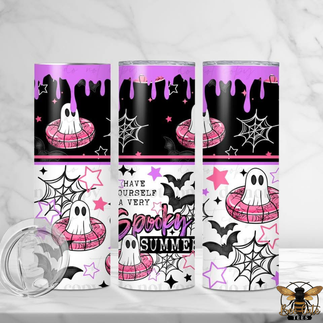 Three skinny tumblers with a Halloween-themed 'Spooky Summer' design, featuring purple and black dripping graphics, white ghosts in pink floaties, black bats, spiderwebs, and stars. A clear lid is shown in the foreground on a white marble surface.