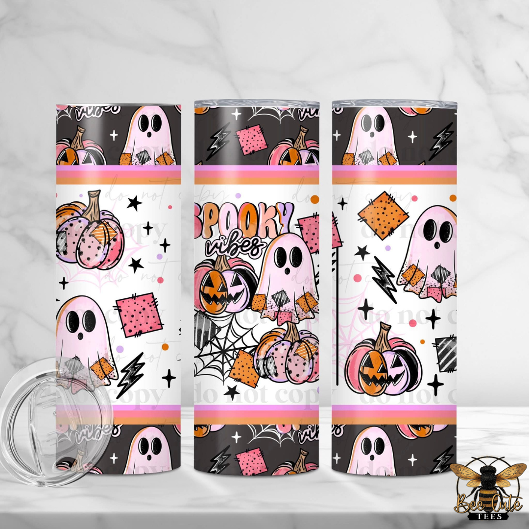 Three slim stainless steel tumblers with a Halloween-themed wrap design, shown on a light marble surface with a clear lid in the foreground. The design features pink ghosts, orange pumpkins, black spiderwebs, and the words 'Spooky Vibes' in pink and orange lettering.