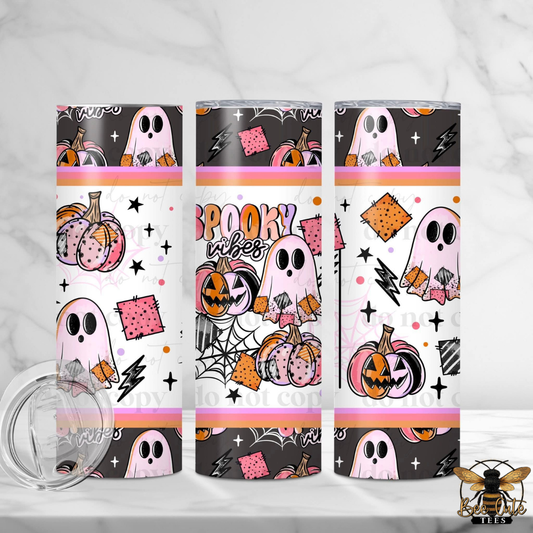 Three slim stainless steel tumblers with a Halloween-themed wrap design, shown on a light marble surface with a clear lid in the foreground. The design features pink ghosts, orange pumpkins, black spiderwebs, and the words 'Spooky Vibes' in pink and orange lettering.