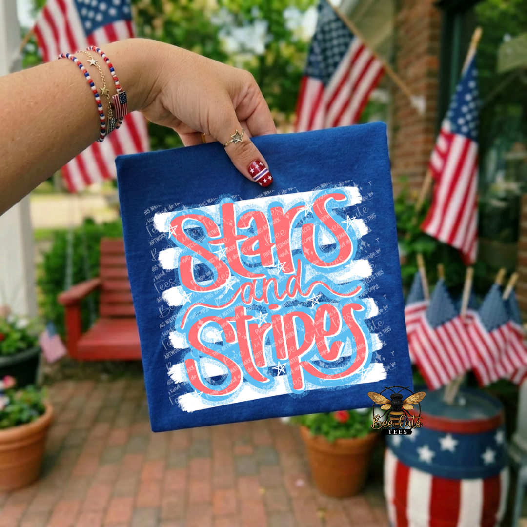 Hand holding a blue t-shirt with 'Stars and Stripes' text in front of American flags.