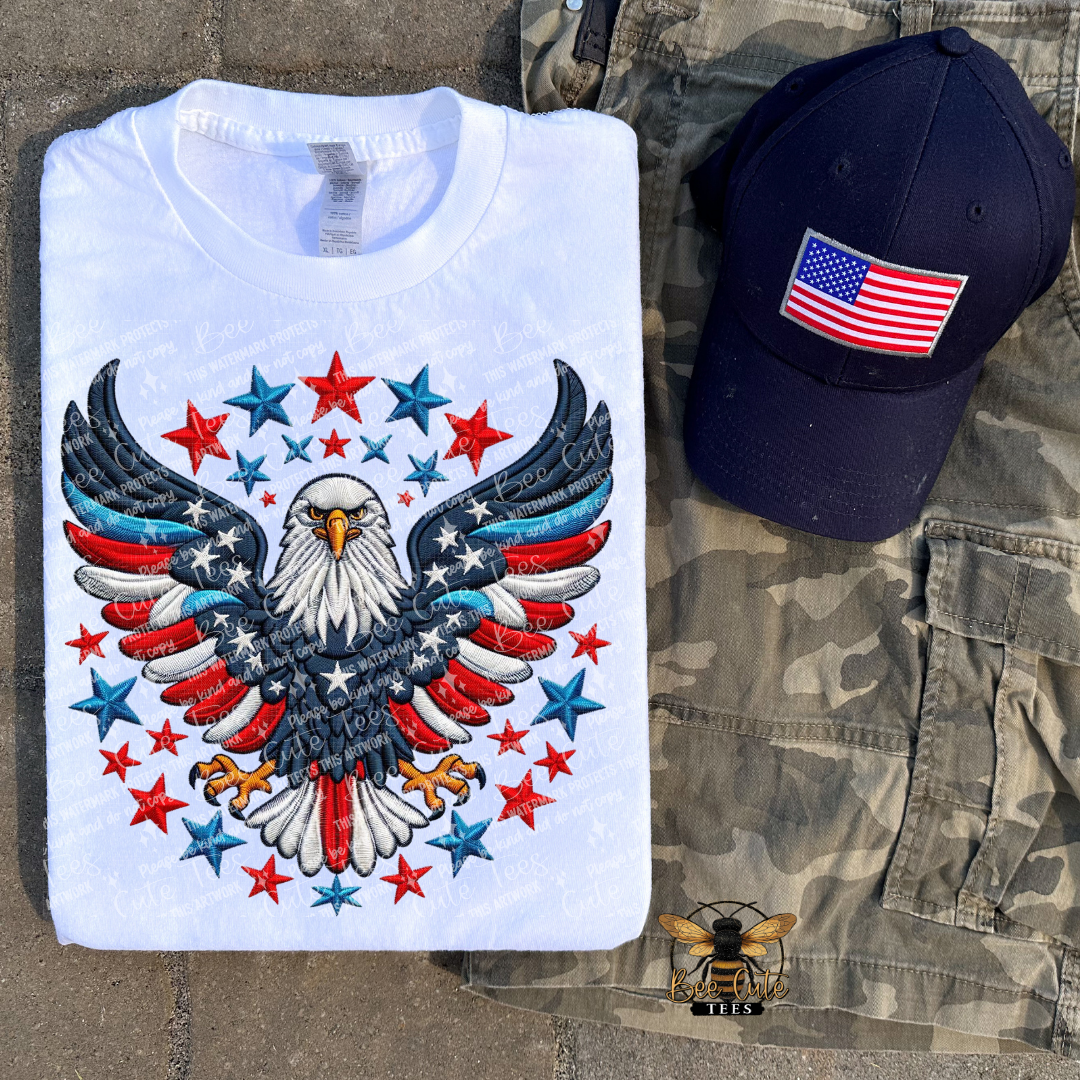 White t-shirt with eagle and star design, navy cap with American flag, camouflage pants on stone surface