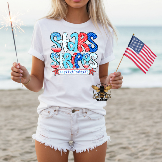 Person wearing a white t-shirt with 'Stars & Stripes' design on a beach