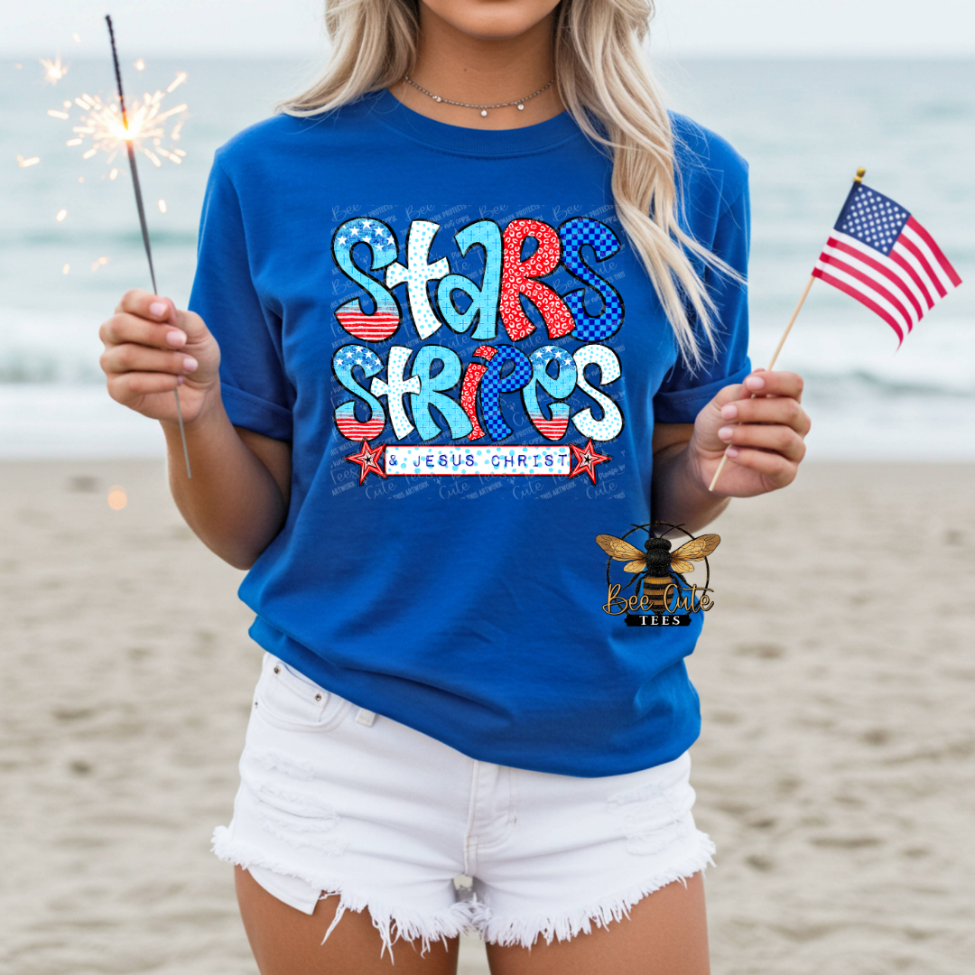 Person wearing a blue t-shirt with 'Stars & Stripes' design on a beach.