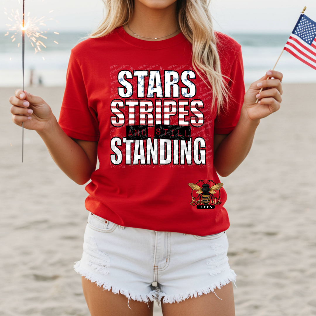 Person wearing a red t-shirt with 'Stars Stripes Standing' text on a beach.
