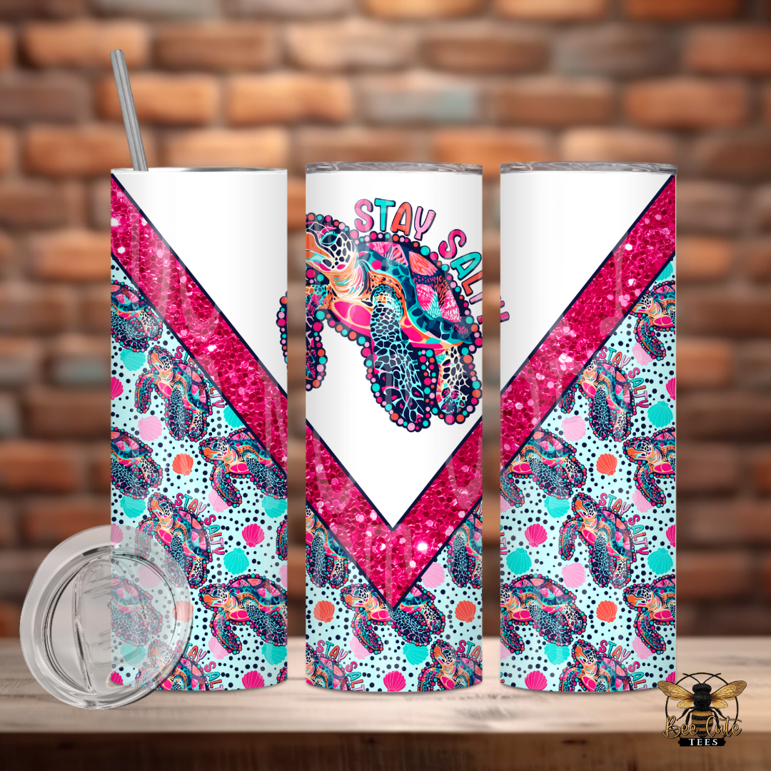 Colorful 20 oz tumbler featuring a vibrant sea turtle and seashell pattern with glitter-inspired pink diagonal accents and “Stay Salty” wording, displayed with a lid and metal straw against a rustic brick background.
