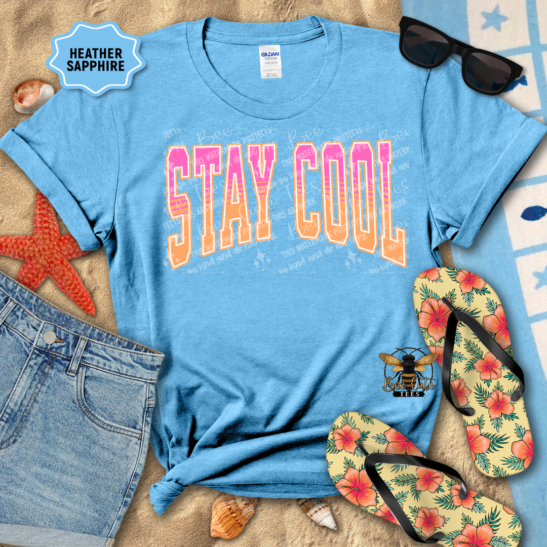 Blue t-shirt with 'STAY COOL' text, sunglasses, flip-flops, and beach items on a sandy background.