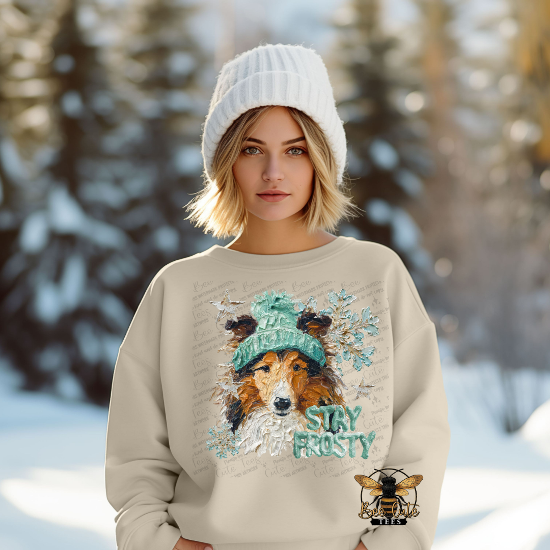 Person wearing a beige sweatshirt with a dog graphic and 'Stay Frosty' text in a snowy forest setting.