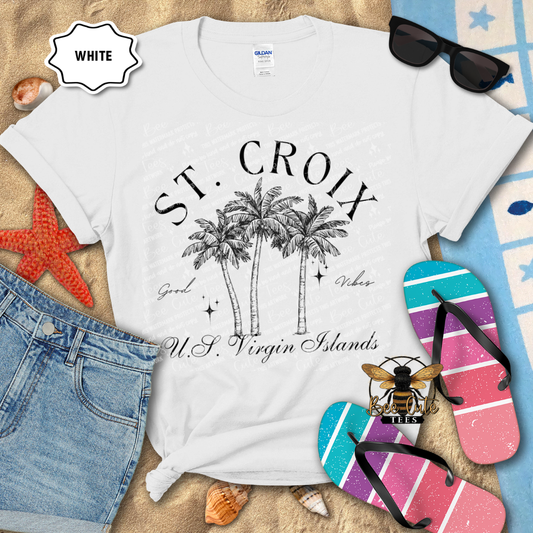 White t-shirt with 'St. Croix' design on a beach-themed background with flip-flops and sunglasses.